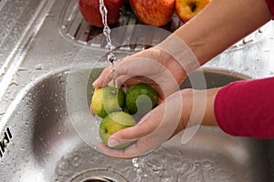 Washing an apple to fight the Coronavirus Outbreak, side view of a person who disinfects an apple by pouring water over it in the photo