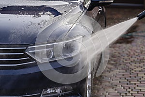 Washing a blue car with high pressure water cleaner, outdoors, closeup