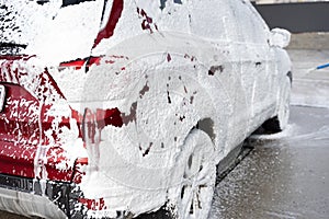 Washing car at autowash . Car wash. red machine under the pressure of water at a car wash. Red car in foam