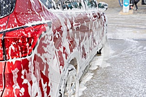 Washing car at autowash . Car wash. red machine under the pressure of water at a car wash. Red car in foam