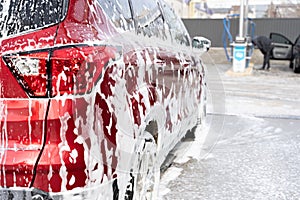 Washing car at autowash . Car wash. red machine under the pressure of water at a car wash. Red car in foam