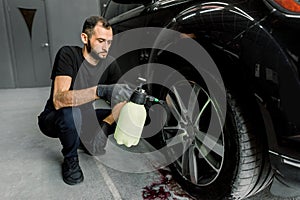 Washing a car in detailing service. Indoor shot of male worker in uniform, washing the car wheels rims with pressure