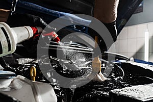 Washing car engine with spray, brush and detergent in detailing auto service. Detailing cleaning motor from dust and