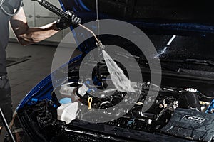 Washing car engine with with water in detailing auto service. Detailing cleaning motor from dust and dirt. Pouring water