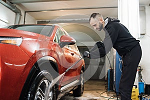 Close up of red car wheel indoor. Smiling bearded man washing red car with water jet.