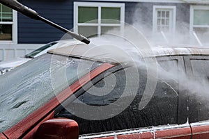 During the washing of a car, a man sprays water with high pressure jets to clean the vehicle