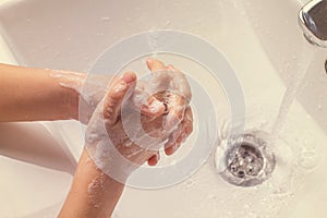 Washing children`s soapy hands under running water in the sink