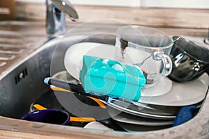 Washing dishes by hand. Pile of dirty dishes and soapy sponge in stainless steel kitchen sink