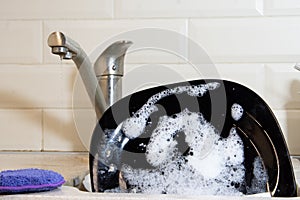 Washing dishes in the kitchen. Dirty dishes plates and glasses, lie in the sink in white foam front view. homework