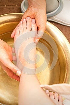 Washing female foot in a special container by male masseur in spa salon.