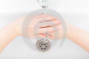 Washing femle hands in white ceramic washbasin with a chrome faucet.