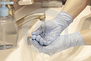 Washing hands in medical gloves under the faucet with water