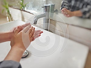 Washing hands with soap in the bathroom sink at home to prevent viruses and bacterias.
