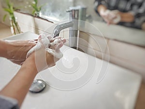 Washing hands with soap in the bathroom sink at home to prevent viruses and bacterias.