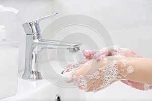 Washing hands with soap under the faucet with water.