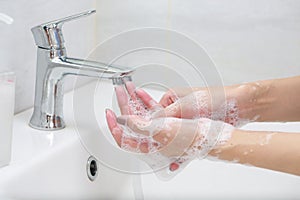 Washing hands with soap under the faucet with water.