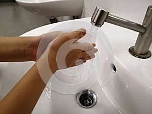 Washing hands under flowing tap water.