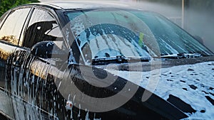 Washing luxury black car on touchless car wash. Cleaning the details of car. Washing sedan car with foam self-service