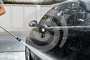 Washing luxury black car on touchless car wash. Cleaning the details of car. Washing sedan car with foam self-service