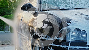 Washing luxury black car on touchless car wash. Cleaning the details of car. Washing sedan car with foam self-service