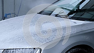 Washing luxury silver car on touchless car wash. Washing sedan car with foam self-service and high pressure water
