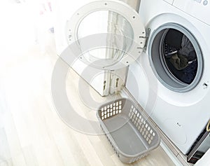 A washing machine with the door open and a small plastic basket to hold the freshly washed laundry