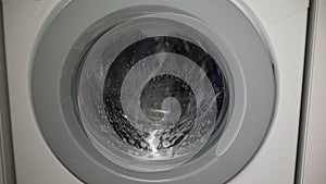 The washing machine washes clothes. The washing machine drum is rotating.