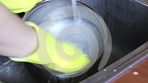 Washing pan in kitchen sink with soap and water by hands in yellow rubber glowes