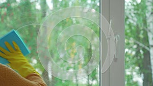 Washing a plastic window in the summer. A woman`s hand in yellow rubber gloves washes the window with a cleaning agent, a blue rag