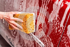 Washing a red car with a foamy yellow sponge. Woman& x27;s hand washing a car at the car wash