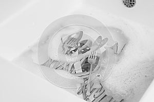 Washing silver spoons, forks and knives in kitchen sink with foam, above view