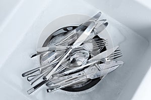 Washing silver spoons, forks and knives in kitchen sink with foam, flat lay