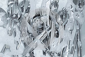 Washing silver spoons, forks and knives in kitchen sink with foam, flat lay