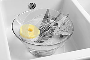 Washing silver spoons, forks and knives in kitchen sink