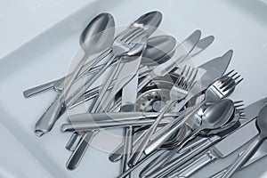 Washing silver spoons, forks and knives in kitchen sink with water, above view