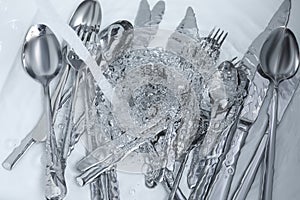 Washing silver spoons, forks and knives under stream of water in kitchen sink, top view