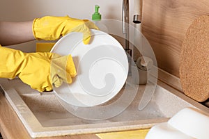 washing-up and housekeeping concept - close up of woman hands in protective gloves washing dishes with sponge at home kitchen