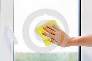 Washing a window pane with a yellow microfiber cloth, close-up with a blurred background
