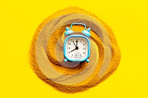 Waste of time concept. Clock on sand on yellow background top-down
