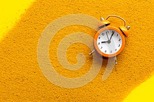 Waste of time concept. Clock on sand on yellow background top-down copy space