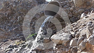 Waste water flows out of a sewage pipe into a sandy hole