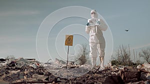 Wastes of human life, woman in uniform and protective glasses holding poster think green standing at landfill in boots