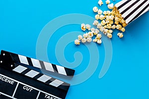 Watch film in cinema with popcorn and clapperboard on blue background top view