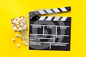 Watch film in cinema with popcorn and clapperboard on yellow background top view