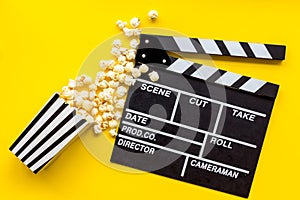 Watch film in cinema with popcorn and clapperboard on yellow background top view