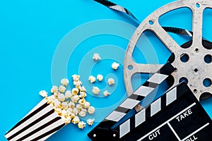 Watch film in cinema with popcorn, video tape and clapperboard on blue background top view