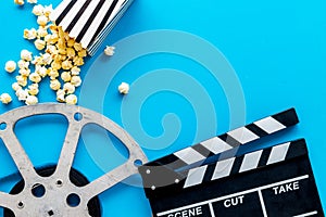 Watch film in cinema with popcorn, video tape and clapperboard on blue background top view