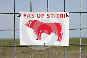 Watch out for bulls sign with red bull and dutch text on a fence.