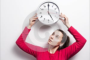 Watch the time concept. The girl is holding round classic watch over her head. Young brunette woman is looking at clock