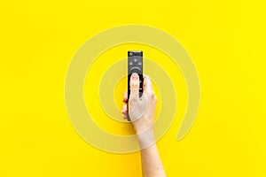 Watch TV concept. TV remote in hand on yellow background top-down copy space